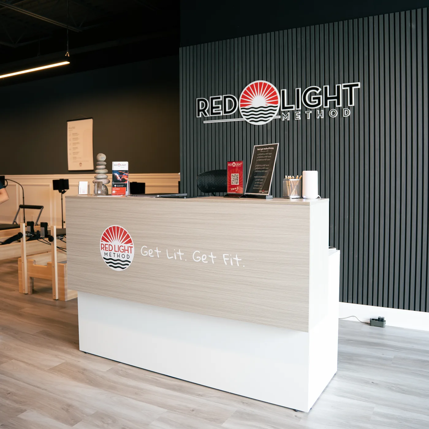 The front desk at Red Light Method Commack, with the studio logo on a black slat wall behind it and Get Lit. Get Fit. lettered on the desk